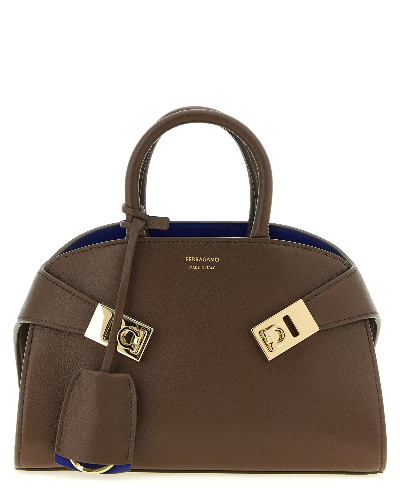A brown leather handbag by Ferragamo with gold-tone hardware and a blue interior lining, shown against a plain white background.