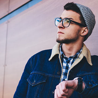 Person wearing glasses and a beanie against a wooden wall