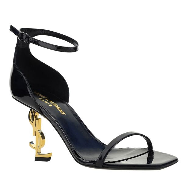 A black patent leather high-heeled sandal with an ankle strap, a low square toe, and a signature gold YSL metal heel, shown on a plain white background.