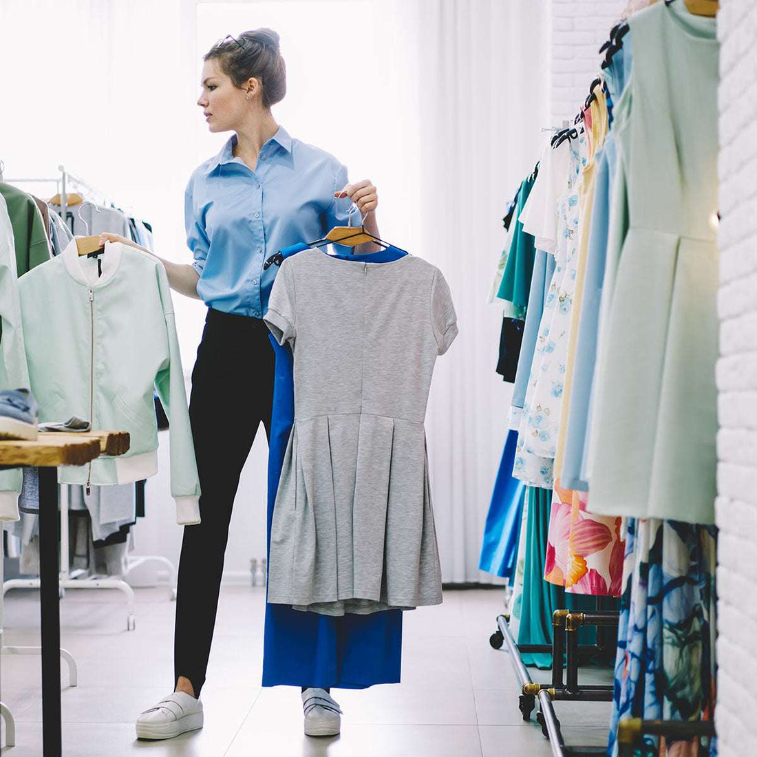 Woman shopping in a clothing store holding two hangers with clothes.