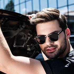 Man wearing sunglasses and a black shirt, holding a car door open.